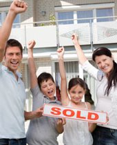 Recent home buyers in front of house with sold sign