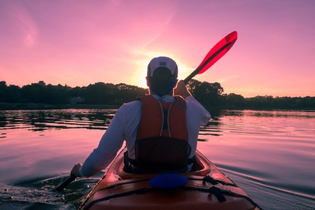 Man kayaking on a lake at sunset.