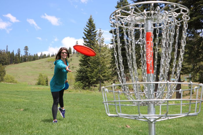 Disc golfer throwing toward a basket in a forest meadow
