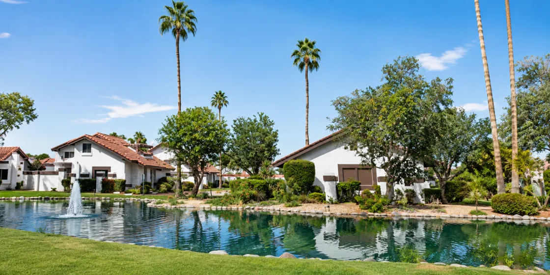 a manmade lake and bridge with tall palm trees and green grass on a sunny day at scottsdale park villas colndols and townholmes at mccormick ranch in scottsdale